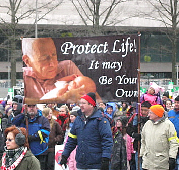 Banner, showing elderly man who holds baby, urges: 'Protect Life! It May Be Your Own'