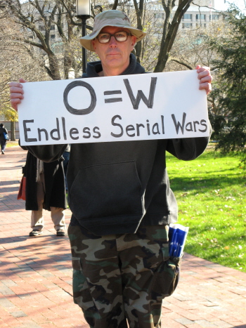 Man in combat fatigues holds sign that says 'O=W/Endless Serial Wars'