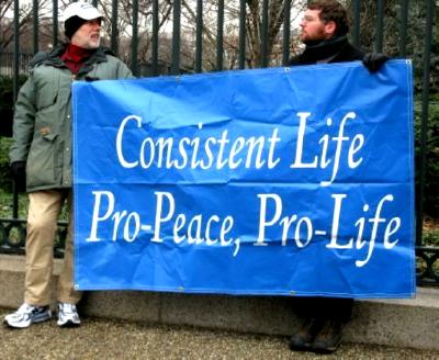 Two men hold banner that proclaims: 'Consistent Life/
Pro-Peace, Pro-Life'
